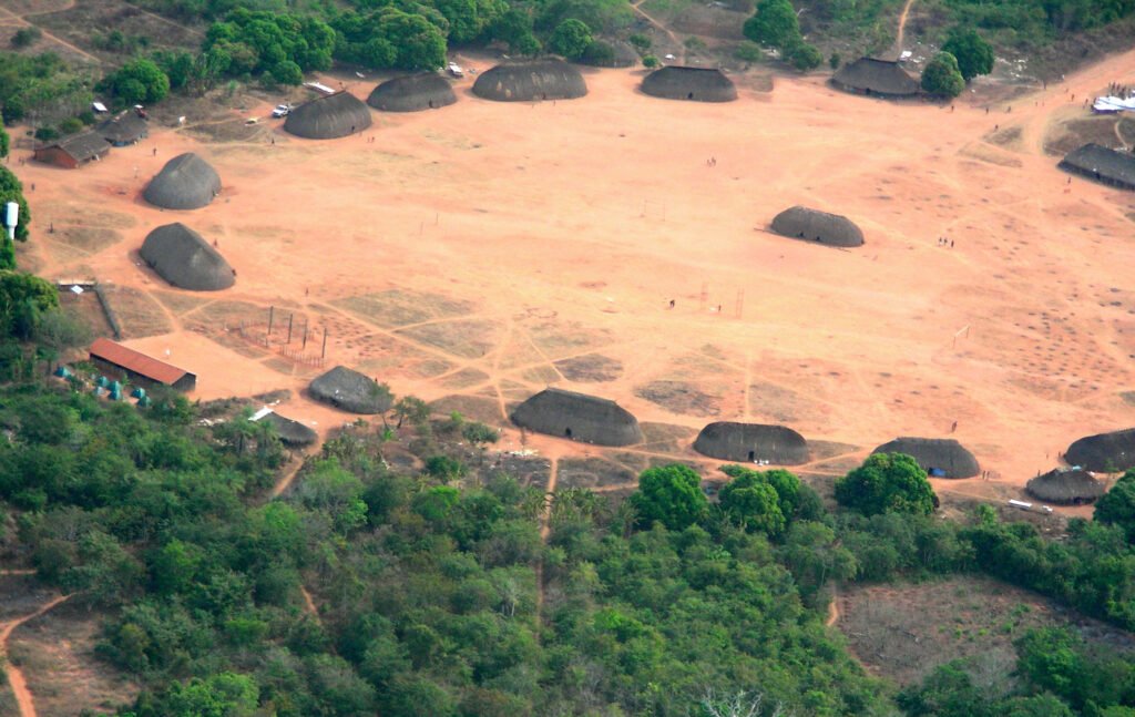 Vista aérea do Parque Indígena do Xingu, com casas tradicionais circulares cercadas pela floresta amazônica.
