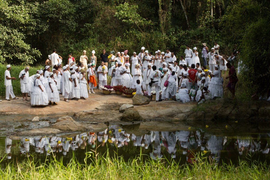 Grupo de pessoas vestidas de branco realiza celebração religiosa às margens de um rio no Quilombo dos Palmares, em Alagoas.